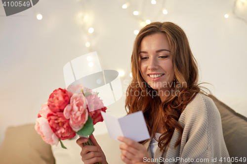 Image of happy woman with flowers and greeting card at home