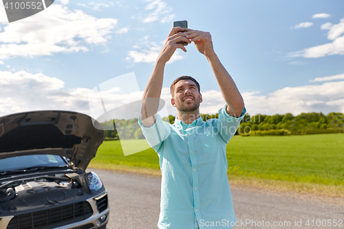 Image of man with smartphone and broken car at countryside