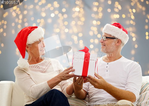 Image of happy senior couple in santa hats with gift box