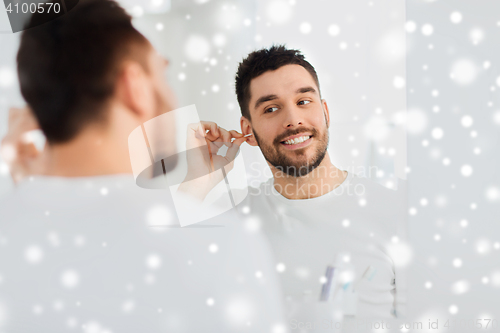 Image of man cleaning ear with cotton swab at bathroom