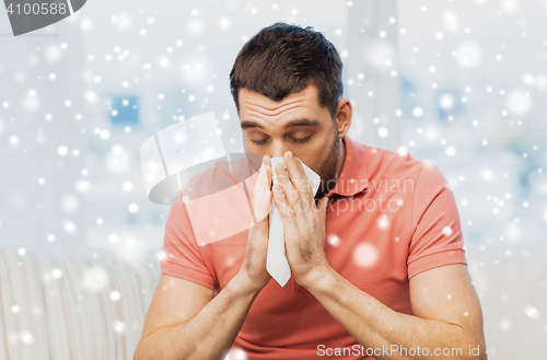 Image of sick man blowing nose to paper napkin at home