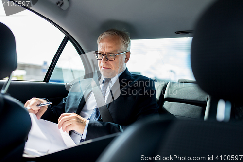 Image of senior businessman with papers driving in car