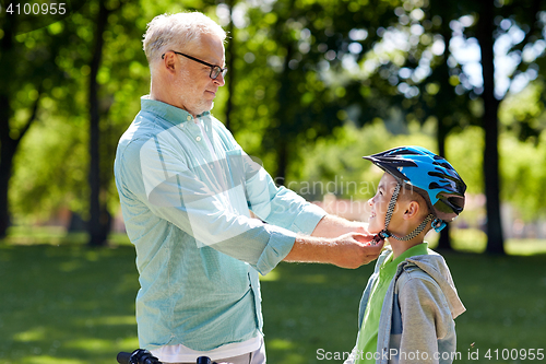 Image of old man helping boy with bike helmet at park