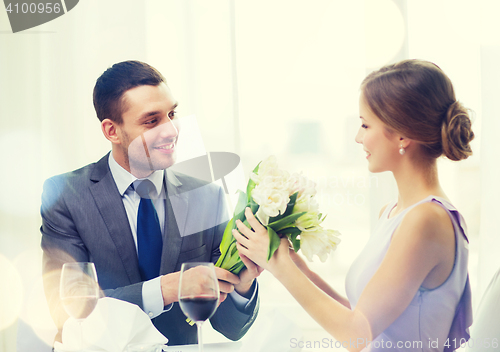 Image of smiling man giving flower bouquet at restaurant