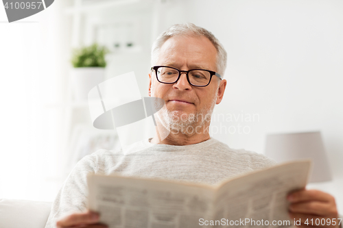 Image of senior man in glasses reading newspaper at home