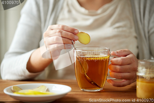Image of close up of woman adding ginger to tea with lemon