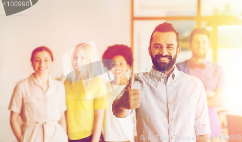 Image of happy man showing thumbs up over team in office