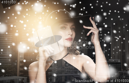 Image of beautiful woman in black hat over city and snow