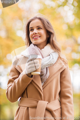 Image of happy young woman drinking coffee in autumn park