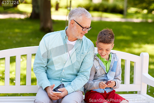 Image of old man and boy with smartphones at summer park