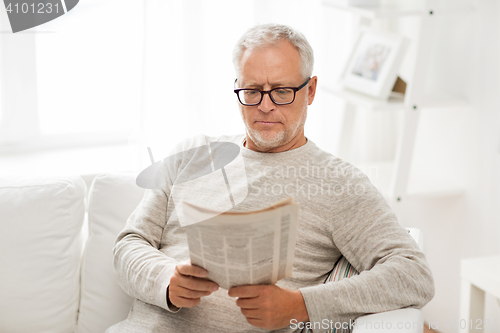 Image of senior man in glasses reading newspaper at home