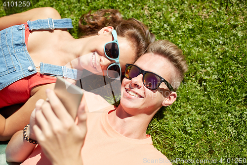 Image of happy teenage couple smartphone lying on grass