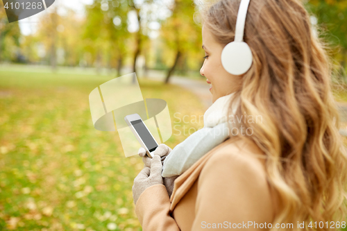 Image of woman with smartphone and earphones in autumn park