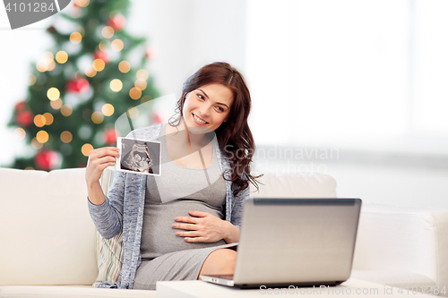 Image of happy pregnant woman with ultrasound image at home