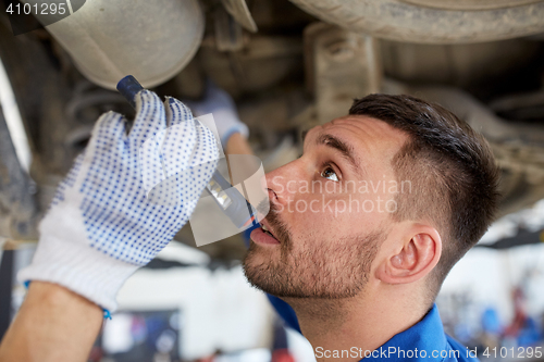 Image of mechanic man with flashlight repairing car at shop