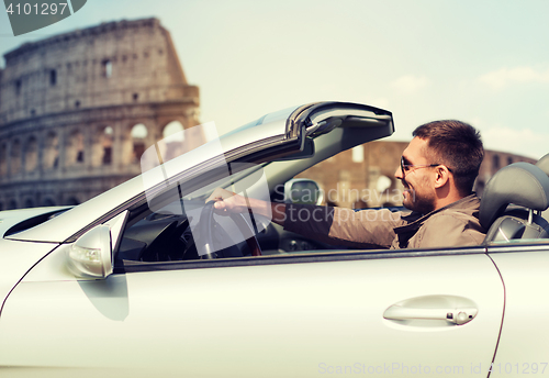 Image of happy man driving cabriolet car over coliseum