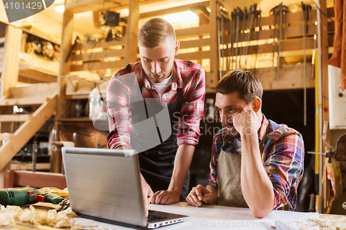 Image of carpenters with laptop and blueprint at workshop