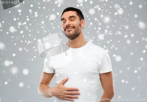 Image of happy full man touching tummy over snow background