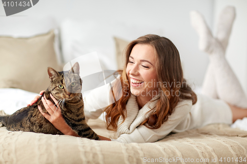 Image of happy young woman with cat lying in bed at home