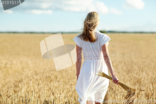 Image of young woman with cereal spikelets walking on field