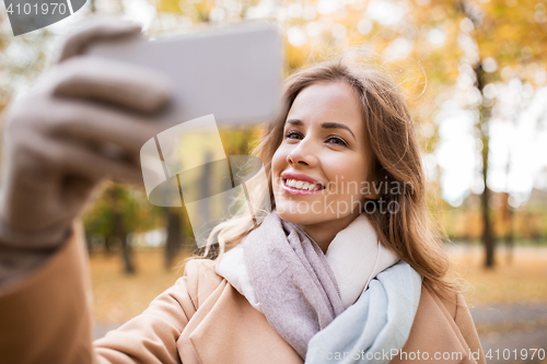 Image of woman taking selfie by smartphone in autumn park