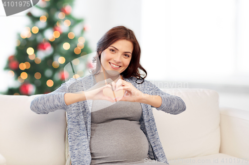 Image of happy pregnant woman making heart gesture at home