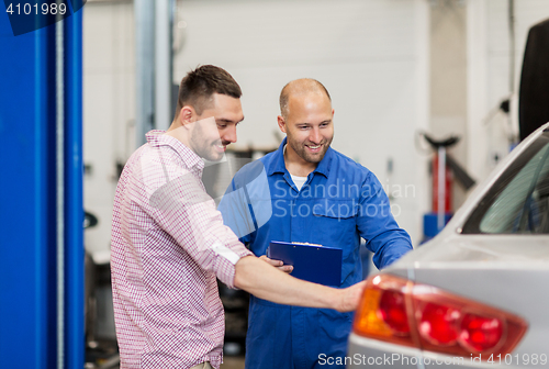 Image of auto mechanic with clipboard and man at car shop