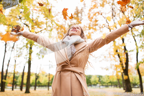 Image of happy woman having fun with leaves in autumn park