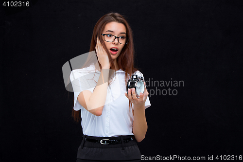 Image of The young business woman with alarm clock on black background