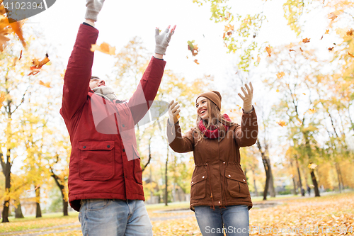 Image of happy young couple throwing autumn leaves in park