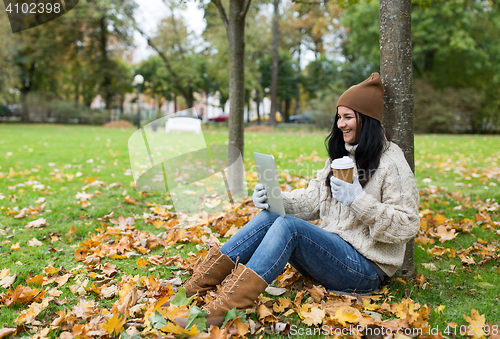 Image of woman with tablet pc and coffee in autumn park
