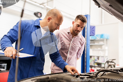 Image of auto mechanic with clipboard and man at car shop