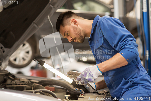 Image of mechanic man with lamp repairing car at workshop