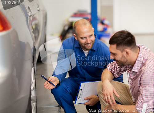 Image of auto mechanic with clipboard and man at car shop