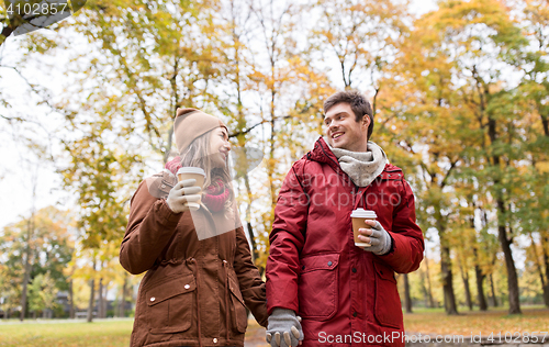 Image of happy couple with coffee walking in autumn park