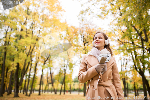 Image of woman with smartphone and earphones in autumn park