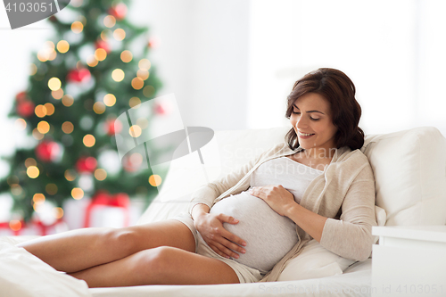 Image of happy pregnant woman lying on bed at christmas