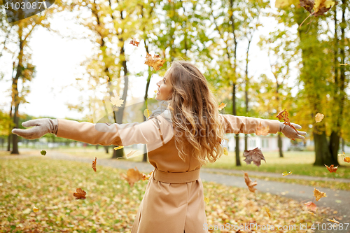 Image of happy woman having fun with leaves in autumn park