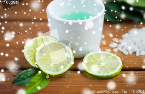 Image of close up of body lotion in cup and limes on wood