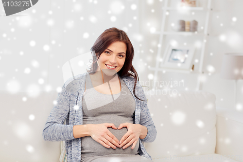 Image of happy pregnant woman making heart gesture at home