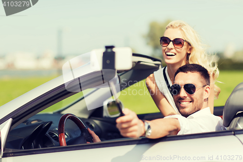 Image of happy couple in car taking selfie with smartphone