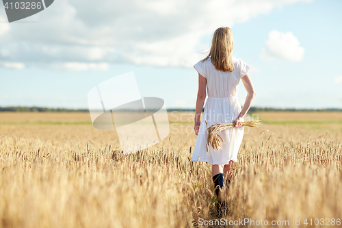 Image of young woman with cereal spikelets walking on field