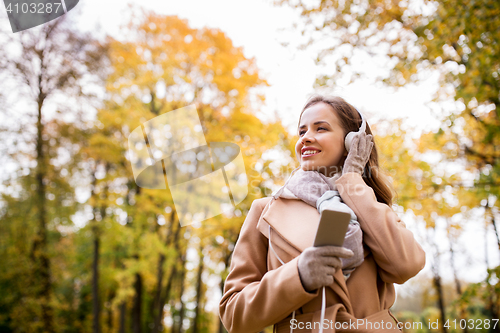 Image of woman with smartphone and earphones in autumn park