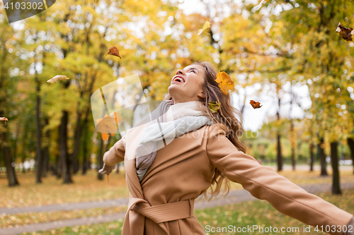 Image of happy woman having fun with leaves in autumn park