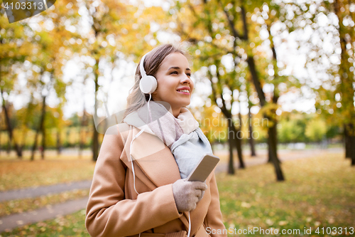 Image of woman with smartphone and earphones in autumn park