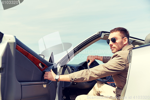 Image of happy man opening door of cabriolet car outdoors