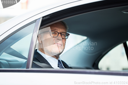 Image of senior businessman driving on car back seat