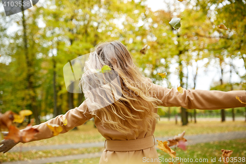 Image of happy woman having fun with leaves in autumn park