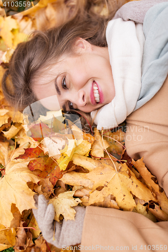 Image of beautiful happy woman lying on autumn leaves
