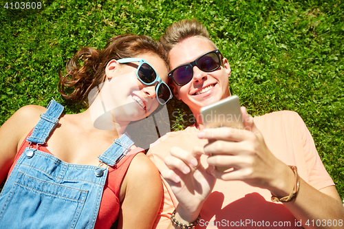 Image of happy teenage couple smartphone lying on grass